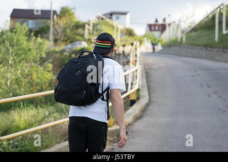 Jeune homme élégant avec un sac à dos marche seul sur une route de montagne Banque D'Images