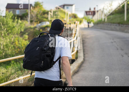 Jeune homme élégant avec un sac à dos marche seul sur une route de montagne Banque D'Images