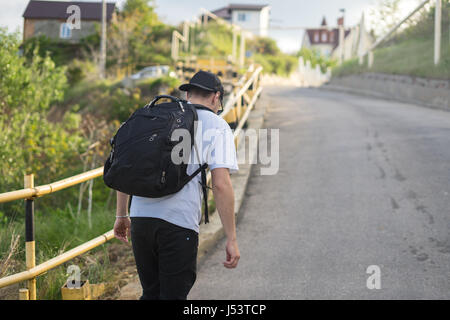 Jeune homme élégant avec un sac à dos marche seul sur une route de montagne Banque D'Images