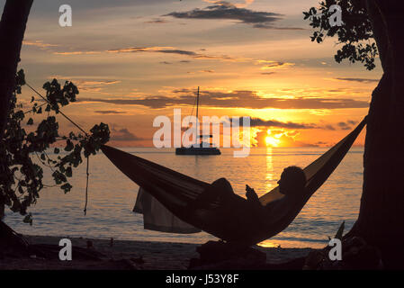 Les vacances à la plage, silhouette d'une femme lisant en hamac au coucher du soleil sur l'île tropicale. Banque D'Images