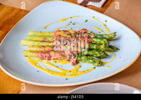 Asperges rôties dans le jambon de Parme en sauce hollandaise et saupoudré de persil Banque D'Images