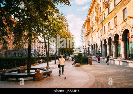 Le Bélarus Minsk. Jeune homme dans des vêtements décontractés, marche sur l'Allée Verte piétonne animée moderne sur la rue Lénine le long bâtiment marron Monumental en été Banque D'Images