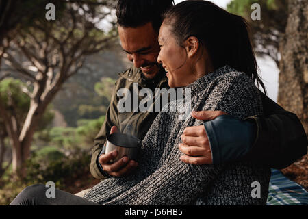 Jeune couple camping en campagne et le café. Jeune homme et femme assis ensemble à l'extérieur et de sourire. Banque D'Images