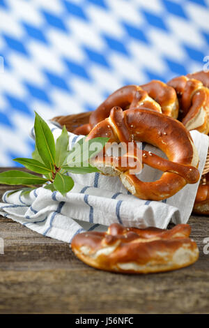 Bretzels bavarois frais dans un grenier sur une table en bois, dans l'arrière-plan le drapeau blanc-bleu de Bavière Banque D'Images