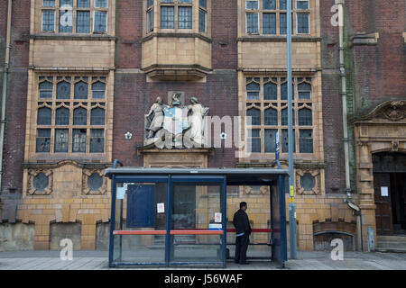 Scène de rue d'un homme attendant à un arrêt de bus devant l'ancien municiple bains de Moseley, Birmingham, Royaume-Uni. Moseley est connu comme l'un des plus quartiers haut de gamme à Birmingham, mais encore montre des signes de ralentissement économique, et le manque d'investissements réguliers et d'entretien général de la zones résidentielles, comme ici sur Moseley Road. Banque D'Images