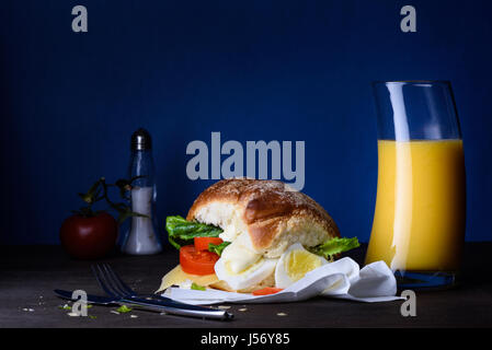 Œufs pochés sandwich pour le petit déjeuner, servi avec du jus d'orange sur la table en bois. Banque D'Images