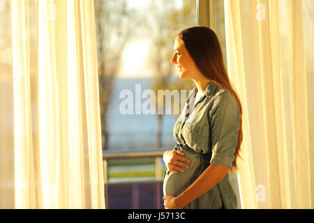 Vue latérale d'une femme enceinte à l'extérieur à travers une fenêtre au coucher du soleil avec une chaleur lumière Banque D'Images