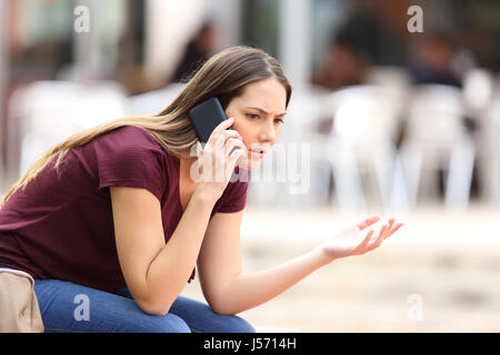 Femme en colère appelant au téléphone assis sur un banc dans la rue Banque D'Images