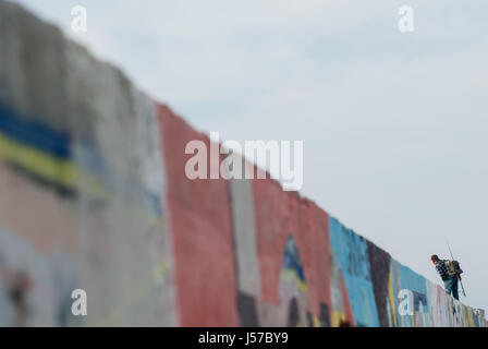 Homme adulte avec une canne à pêche et un sac à dos va à la pêche à pied sur le mur de graffiti à dans la distance Banque D'Images