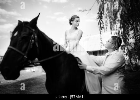 Le marié mène le cheval par la bride. Bride se trouve dans la selle à cheval. Country wedding Banque D'Images