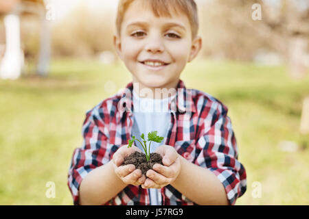 Smiling hazel-eyed boy outdoors holding petit arbrisseau Banque D'Images