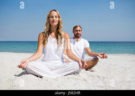 Toute la longueur de smiling couple exerçant alors qu'il était assis sur le sable à la sky Banque D'Images