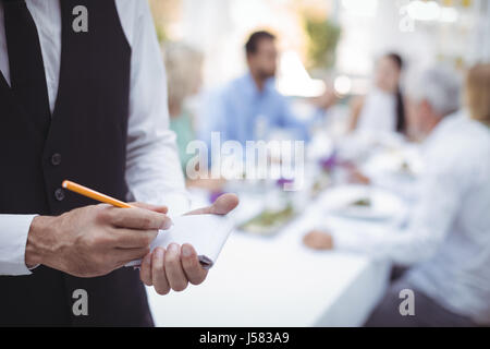 Close-up of waiter writing vue sur le bloc-notes tandis que les amis coin en arrière-plan Banque D'Images