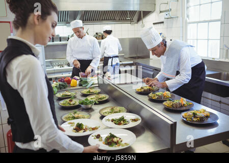 Waitress mets à partir de la commande centrale et chefs preparing food in background Banque D'Images