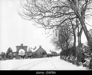 Deux charrettes tirées par des chevaux chargés, chacun tiré par deux chevaux, se propager sur une route couverte de neige passé une porterie et de grandes portes. Arbres couverts de neige sur un remblai de la route sur la gauche. Photographie prise à l'origine en 1900. Restauré à l'aide d'un scan haute résolution prises à partir du négatif original. Banque D'Images