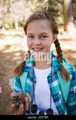 Portrait of smiling girl looking at pine cone dans la forêt Banque D'Images