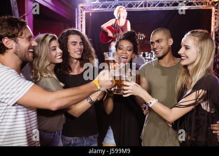 Smiling friends toasting beer glasses avec interprète chantant en arrière-plan at nightclub Banque D'Images