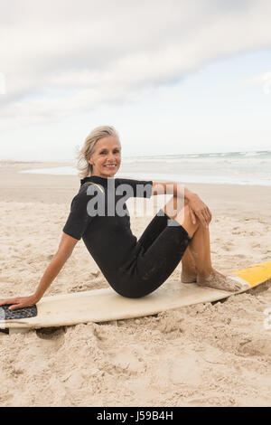 Portrait de femme assise sur une planche de surf contre ciel nuageux Banque D'Images