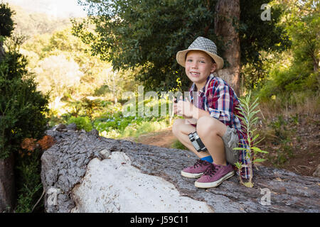 Portrait of smiling boy assis sur le tronc de l'arbre dans la forêt Banque D'Images