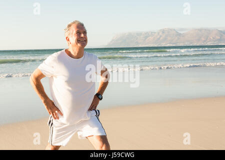 Smiling senior man exercising en se tenant sur le sand at beach Banque D'Images