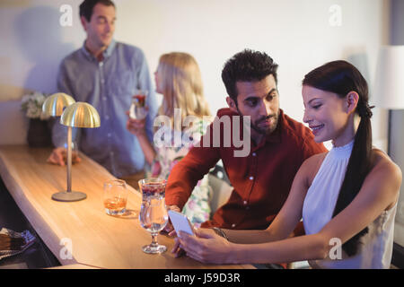 Couple en interaction les uns avec les autres pendant l'utilisation de téléphone mobile au comptoir de restaurant Banque D'Images