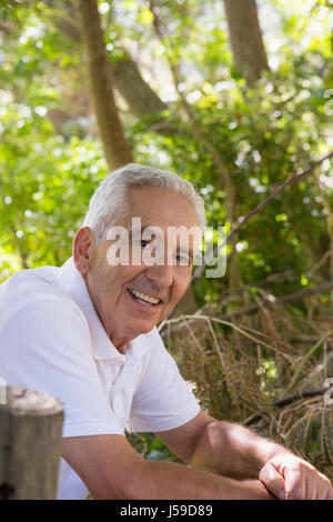 Portrait of smiling senior man leaning on clôture en bois dans la forêt Banque D'Images