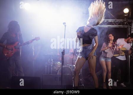 Jeune chanteur avec de longs cheveux ébouriffés performing on stage at nightclub Banque D'Images