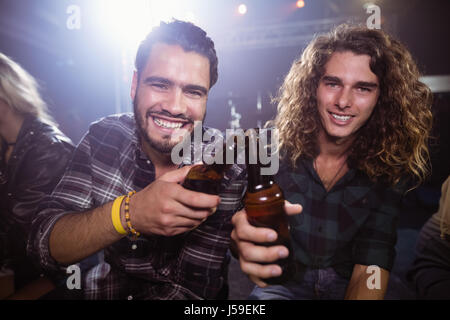 Portrait of male friends toasting beer bottles at nightclub Banque D'Images