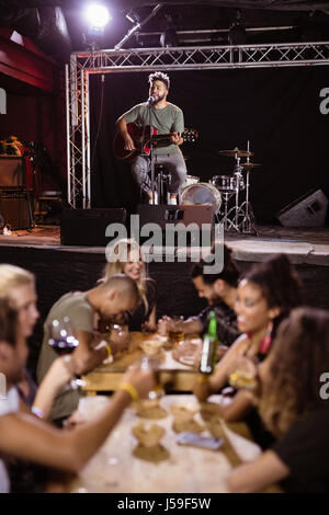 Interprète masculin de chanter sur scène avec fans sitting at table in nightclub Banque D'Images