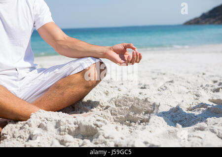 La section basse de l'homme méditant assis sur le sable à la plage Banque D'Images