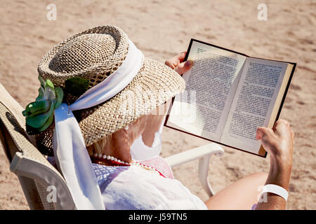 Femme adulte dans un chapeau sur une plage, la lecture d'un livre imprimé. Banque D'Images