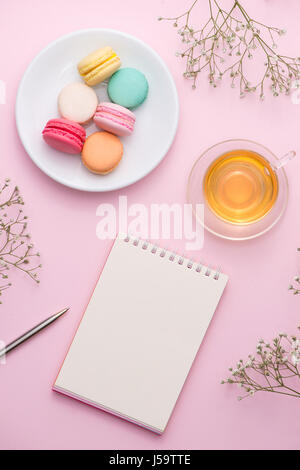 Flatlay d'ordinateur portable, macaron, gâteau de tasse de thé et de fleurs rose sur table. Beau petit déjeuner avec le macaron. Banque D'Images