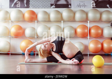 Femme enceinte en noir haut et faire des exercices d'étirement en leggins gym class Banque D'Images
