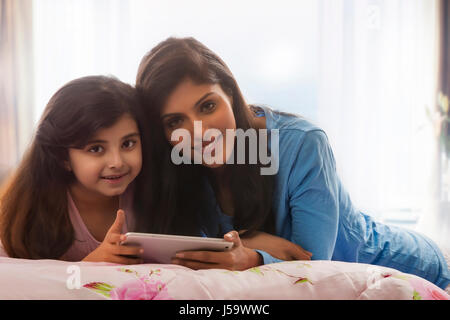 Portrait of smiling mother and daughter Lying in Bed using digital tablet Banque D'Images