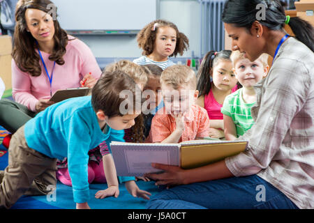 Enseignante en donnant une leçon de pépinière d'étudiants. Ils sont assis sur le sol et il y a un enseignant en prenant des notes. Banque D'Images