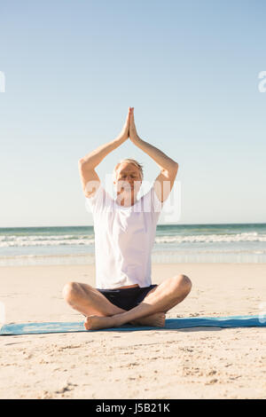 Senior man sitting on mat en méditant at beach Banque D'Images