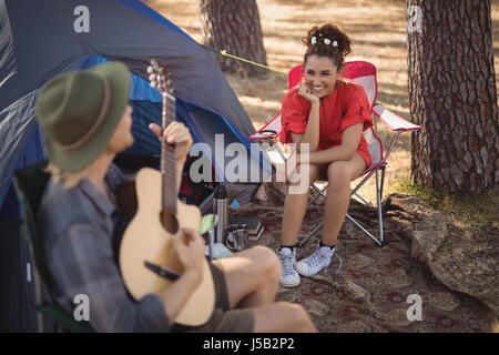 Heureux les jeunes à la recherche de son petit ami à jouer de la guitare par tente à forest Banque D'Images