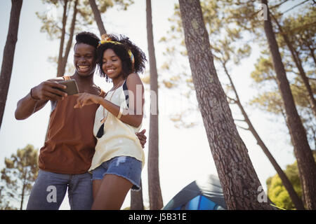 Happy couple using smart phone en position debout par tente à forest Banque D'Images