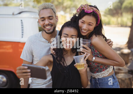 Femme souriante avec des amis en tenant des selfies téléphone mobile alors que l'article de Van sur terrain Banque D'Images