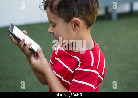 Vue latérale du garçon à l'aide de smart phone while standing at grassy field Banque D'Images