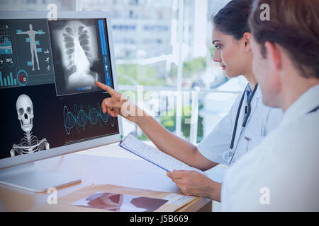 Médecin, pointant sur l'écran d'un ordinateur contre squelette humain avec divers rapports médicaux xray Banque D'Images