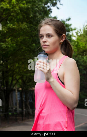 Femme athlétique de l'eau potable, alors que la formation à l'extérieur dans un cadre naturel. Concept d'action et d'un style de vie sain. Banque D'Images