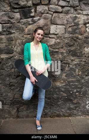 Portrait of a young woman holding skateboard et appuyé contre un mur. Banque D'Images