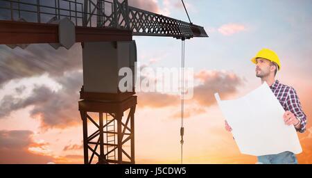 Digital composite of Architect holding blueprint pendant la recherche de crane contre le ciel au coucher du soleil Banque D'Images