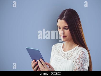 Digital composite de femme aux longs cheveux bruns à l'aide de Tablet PC sur fond bleu Banque D'Images