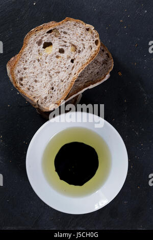 Le pain tranché sur l'ardoise noire avec un bol d'huile d'olive et vinaigre balsamique vinagar. Banque D'Images