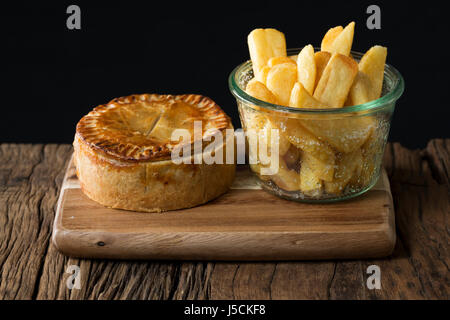 Une tarte de viande britannique traditionnel et frites assis sur une table en bois rustique. Banque D'Images