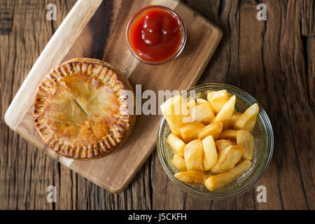 Une tarte de viande britannique traditionnel et frites assis sur une table en bois rustique. Banque D'Images