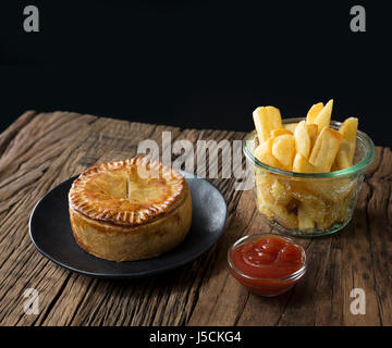 Une tarte de viande britannique traditionnel et frites assis sur une table en bois rustique. Banque D'Images