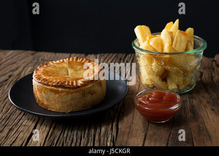 Une tarte de viande britannique traditionnel et frites assis sur une table en bois rustique. Banque D'Images